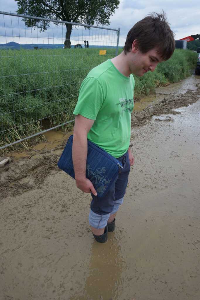 jemand steht im Schlamm der so tief ist, dass er fast in die Gummistiefel läuft