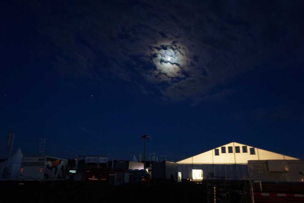 der Mond scheint durch den nächtlichen Wolkenhimmel auf die Zelte