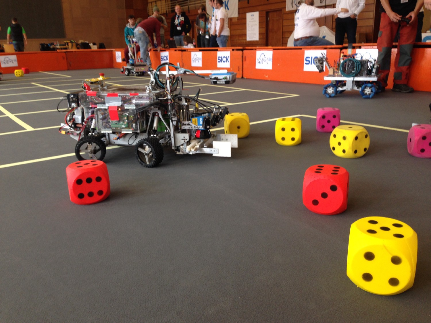 Beteigeuze steht in der Arena des SICK Robot Day 2016. Angebaut sind ein RFID Scanner und eine aufnahme um 15 x 15 cm große, farbige Würfel in der Arena zu sammeln.